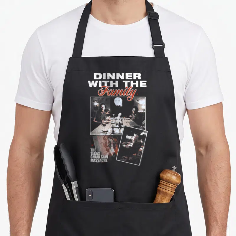 Massacre texas apron - Distressed DINNER WITH THE Family text over three overlapping photos of people at a dinner table — shown on a black cotton canvas apron against a white background