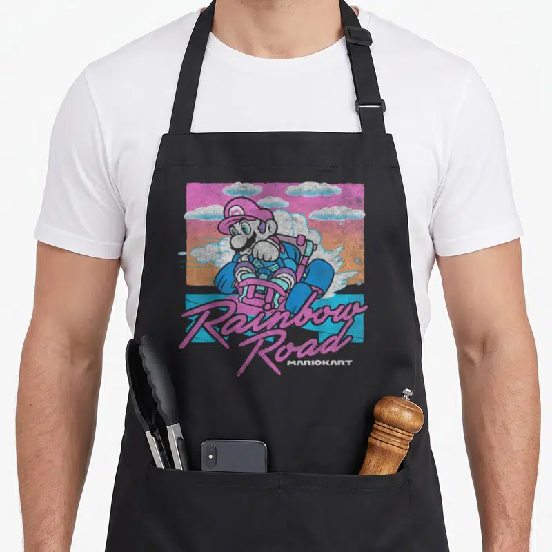 Pastel road apron - Mario in kart with pink Rainbow Road script and MARIOKART text against pastel clouds — shown on a black cotton canvas apron against a white background