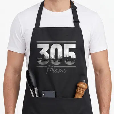 Area florida apron - 305 number filled with cityscape and Miami text in grayscale — shown on a black cotton canvas apron against a white background