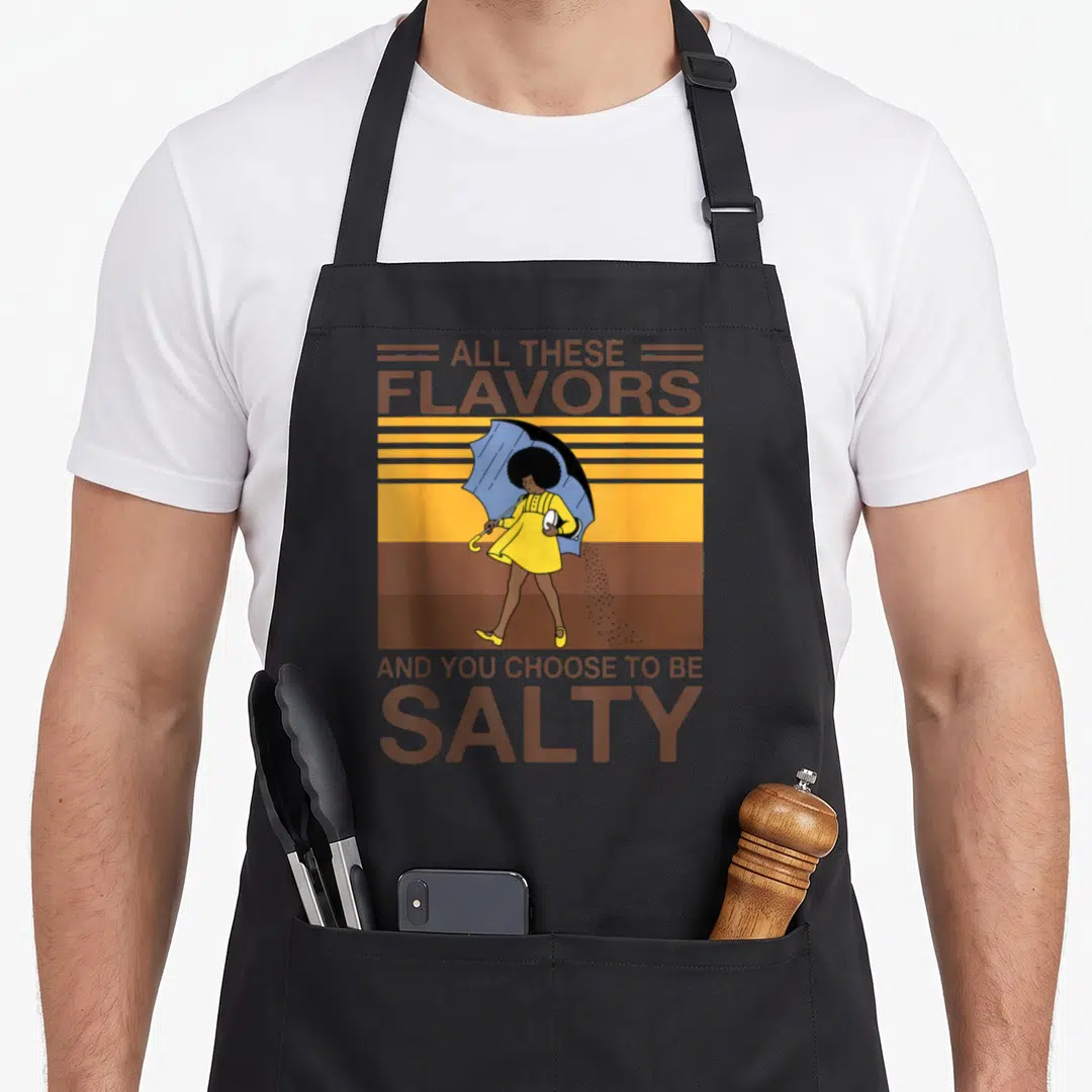 Flavor these apron - Woman in yellow dress holding blue umbrella raining salt with brown text on striped background — shown on a black cotton canvas apron against a white background