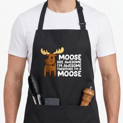 Moose awesome therefore apron - Cartoon brown moose with tan antlers next to stacked white text reading MOOSE ARE — shown on a black cotton canvas apron against a white background
