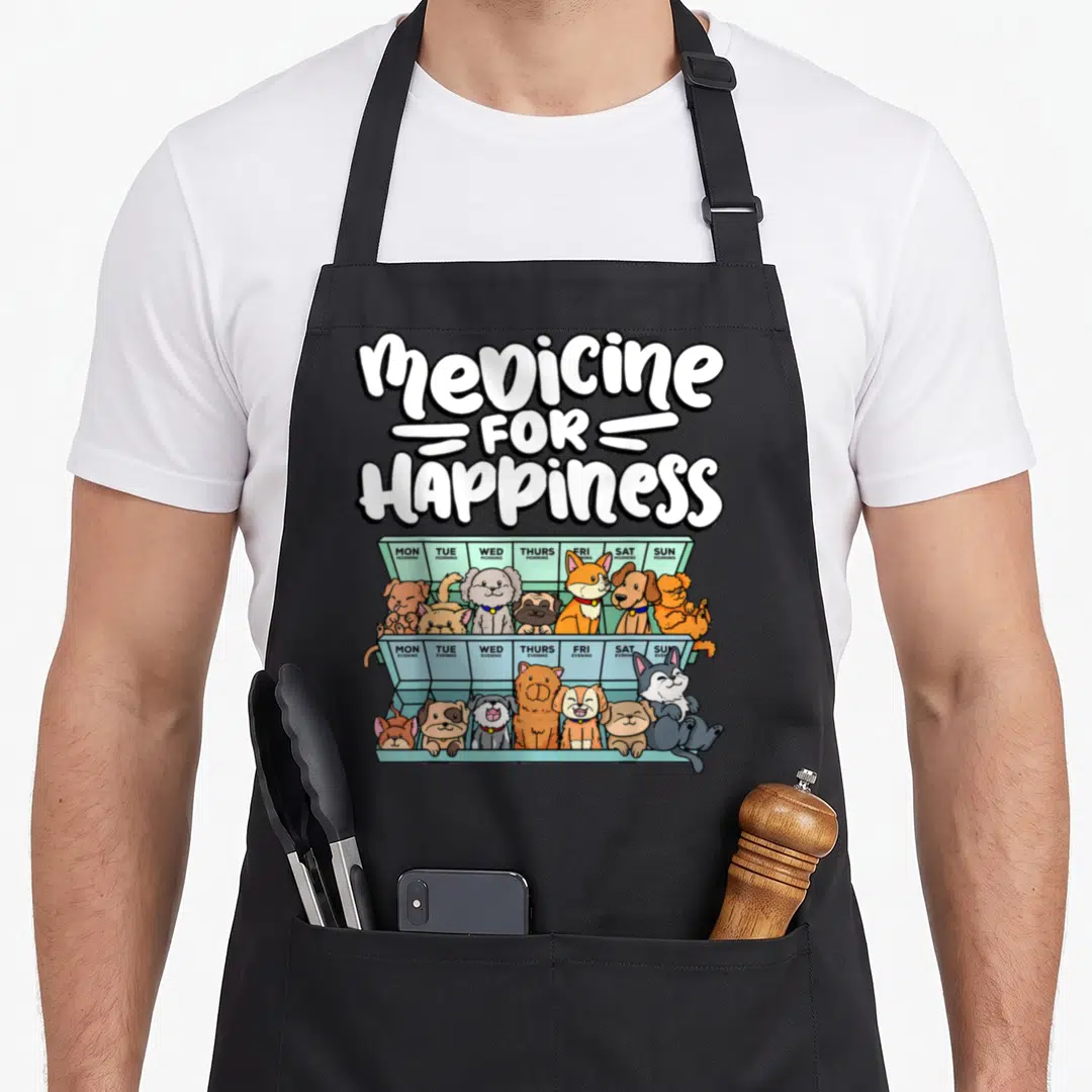Medicine top dog aprons - Cartoon two-tier pill organizer with dogs and cats labeled for every morning and evening — shown on a black cotton canvas apron against a white background