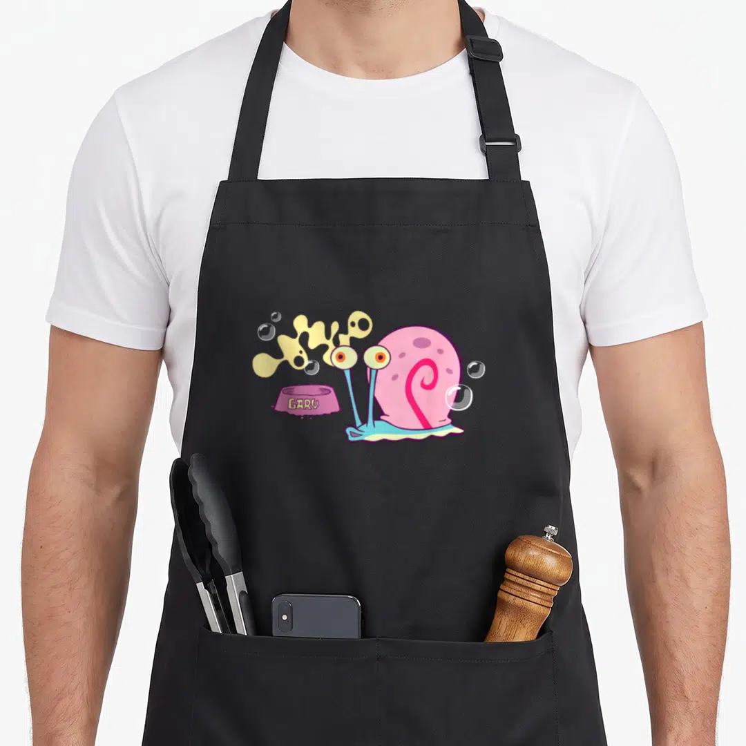 Squarepant snail apron - Pink cartoon snail with GARY bowl, yellow slime, and bubbles on black apron — shown on a black cotton canvas apron against a white background
