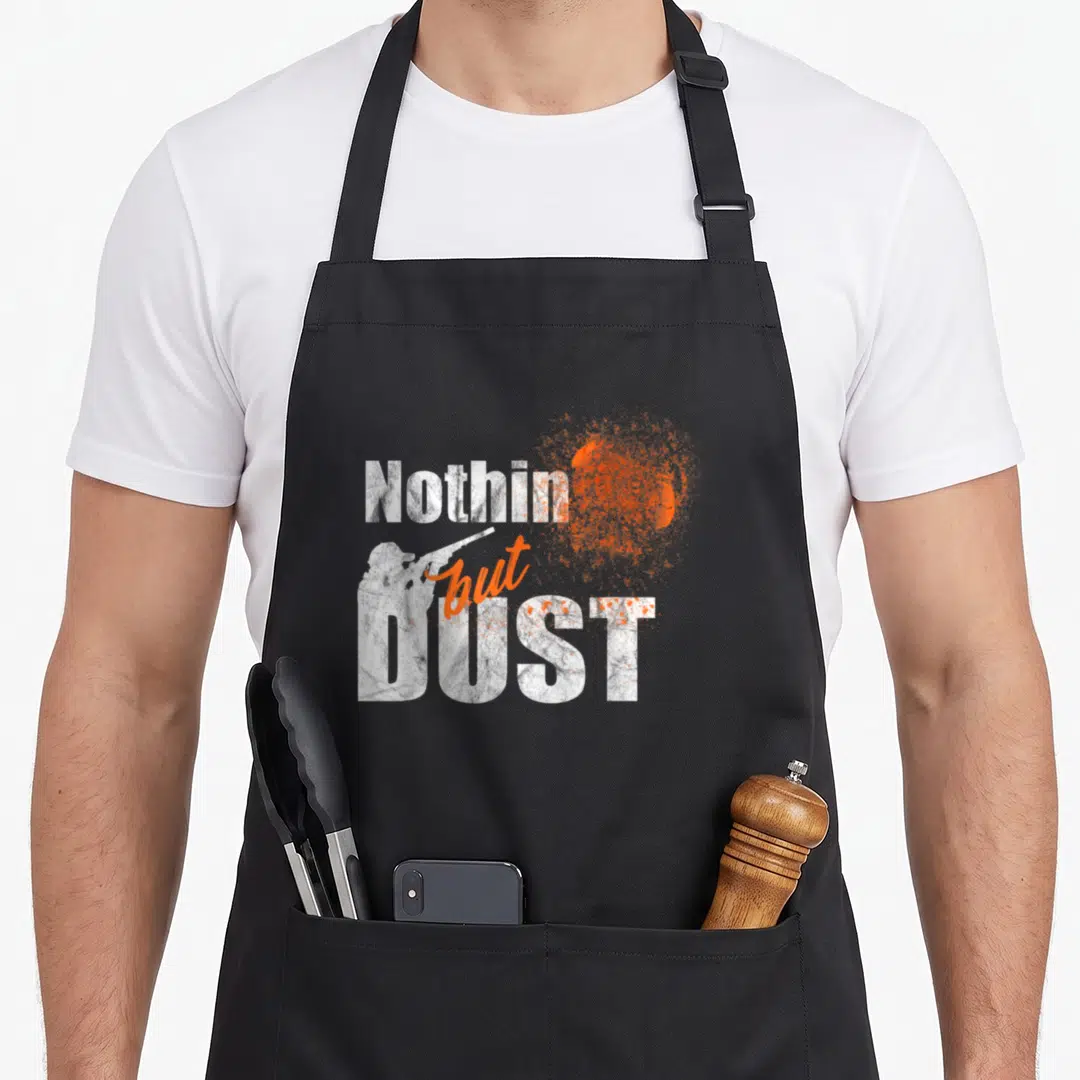 Trap clay apron - Nothin but DUST text with white shooter silhouette and orange exploding clay graphic — shown on a black cotton canvas apron against a white background