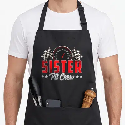 Sister car apron - Speedometer with checkered flags and SISTER in red tire tread font above Pit Crew in silver script — shown on a black cotton canvas apron against a white background