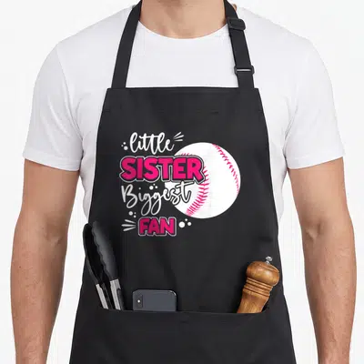 Sibling baseball apron - Stacked text reading little SISTER Biggest FAN over a white baseball with pink stitching — shown on a black cotton canvas apron against a white background