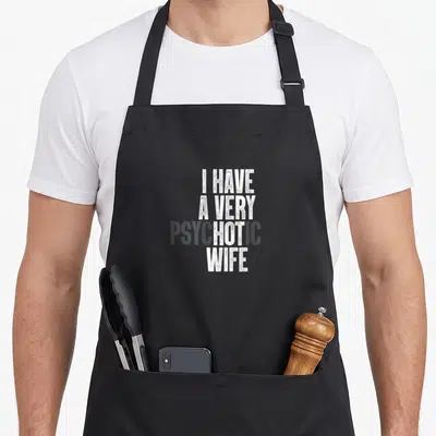 Psychotic husband apron - Stacked white and grey text reading I HAVE A VERY PSYCHOTIC WIFE on grey background — shown on a black cotton canvas apron against a white background