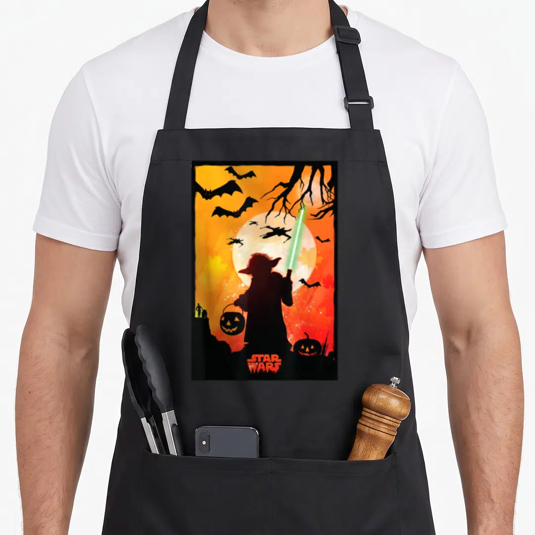 Yoda halloween apron - Yoda silhouette holding green lightsaber and pumpkin bucket against orange moon with TIE fighters — shown on a black cotton canvas apron against a white background