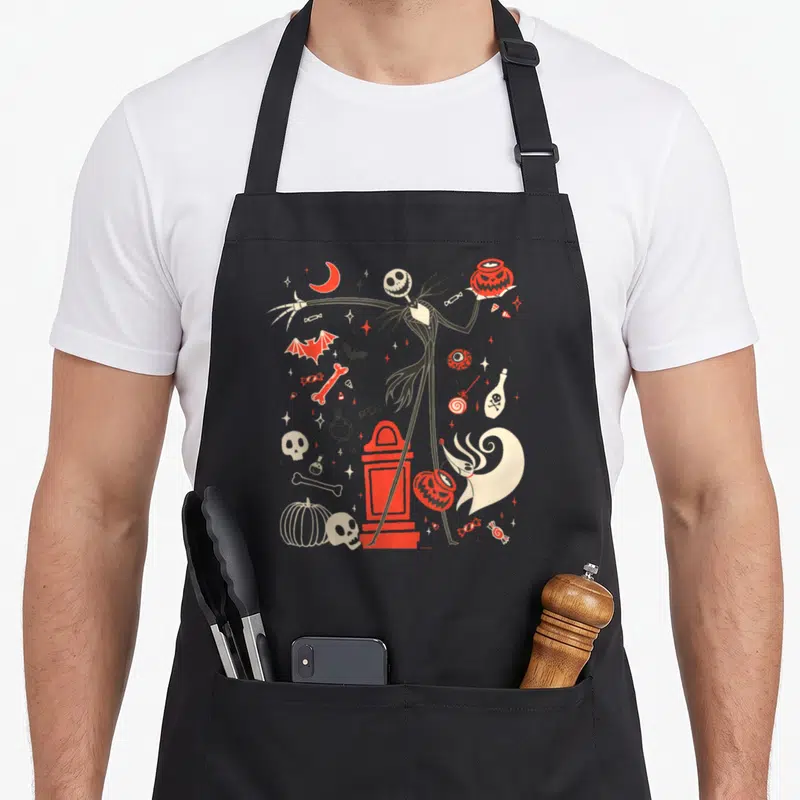 Jack zero halloween apron - Jack Skellleton holding pumpkin bucket surrounded by red moon, candy, and skulls in cartoon — shown on a black cotton canvas apron against a white background