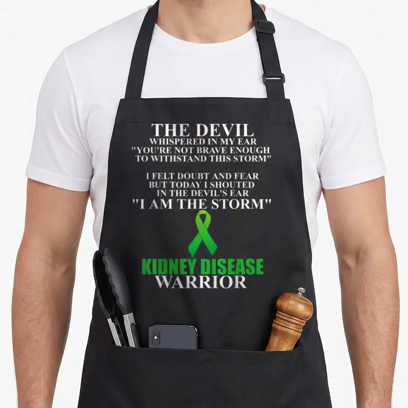 Disease warrior ribbon apron - White and green stacked typography with green kidney awareness ribbon and warrior text — shown on a black cotton canvas apron against a white background