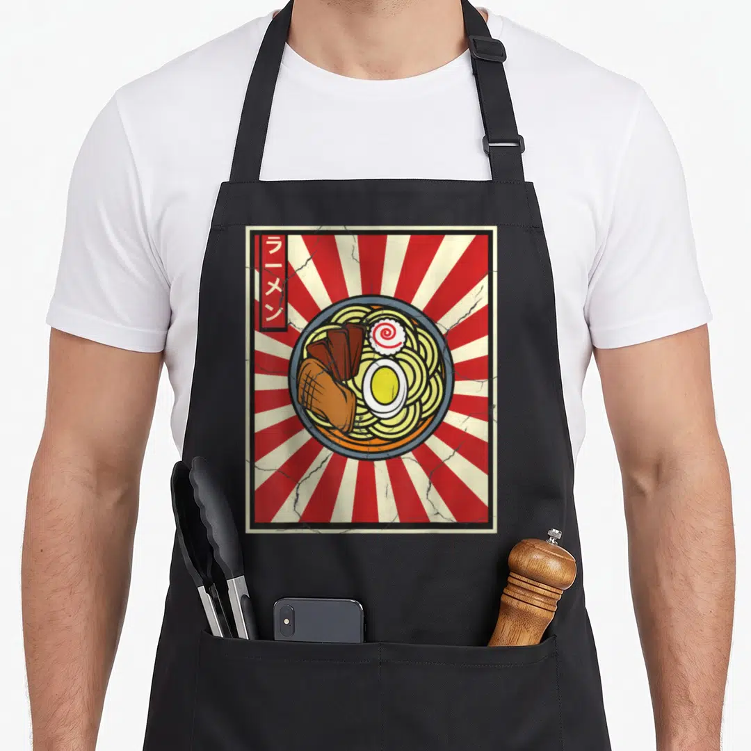 Japanese tasty aprons - Retro ramen bowl with red sunburst background and vertical Japanese text banner on left side — shown on a black cotton canvas apron against a white background