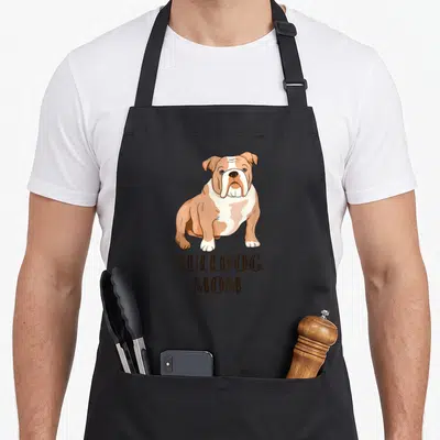 Vintage bulldog english aprons - Cartoon bulldog sitting above stacked BULLDOG MOM text in dark brown lettering — shown on a black cotton canvas apron against a white background