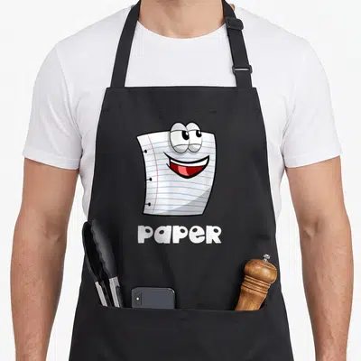 Scissor halloween paper apron - Cartoon white lined paper sheet with face and bold paper text — shown on a black cotton canvas apron against a white background