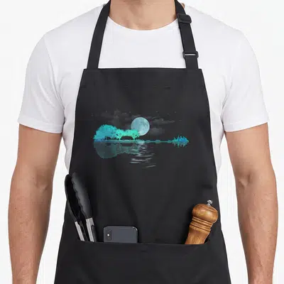 Lake guitar teacher apron - Cyan moon over trees and city skyline reflected in water — shown on a black cotton canvas apron against a white background