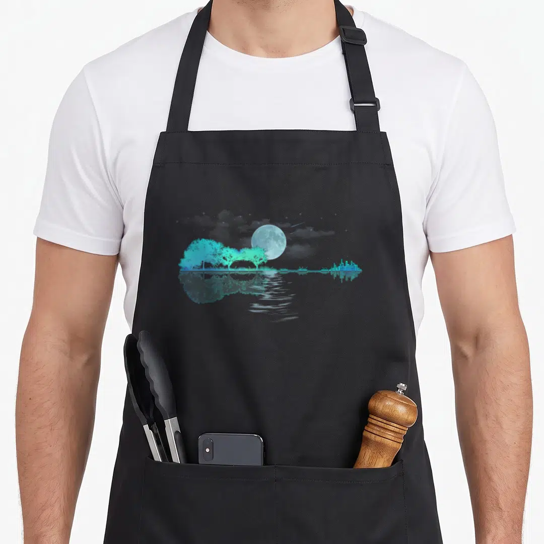 Lake guitar teacher apron - Cyan moon over trees and city skyline reflected in water — shown on a black cotton canvas apron against a white background