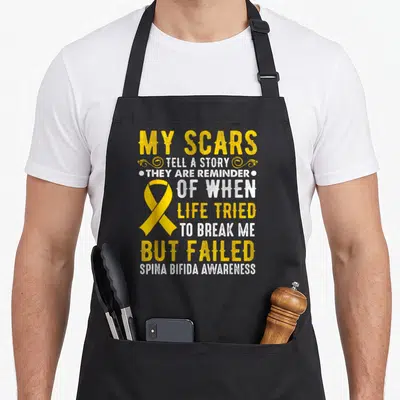 Survivor spina bifida awareness apron - Yellow ribbon and distressed text reading My Scars Tell A Story Spina Bifida — shown on a black cotton canvas apron against a white background