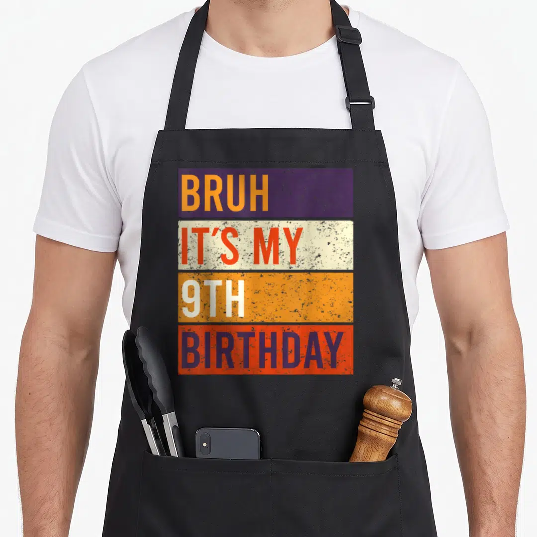 Vintage bruh birthday apron - Stacked text BRUH IT'S MY 9TH BIRTHDAY on purple orange red white blocks — shown on a black cotton canvas apron against a white background