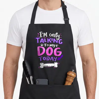 Talking dog apron - Stacked pink purple and white text reading I'M only TALKING TO MY DOG TODAY above a white bone — shown on a black cotton canvas apron against a white background