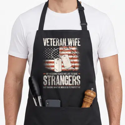 Veteran wife best husband apron - Two dog tags over distressed US flag with quote about husband protecting wife — shown on a black cotton canvas apron against a white background
