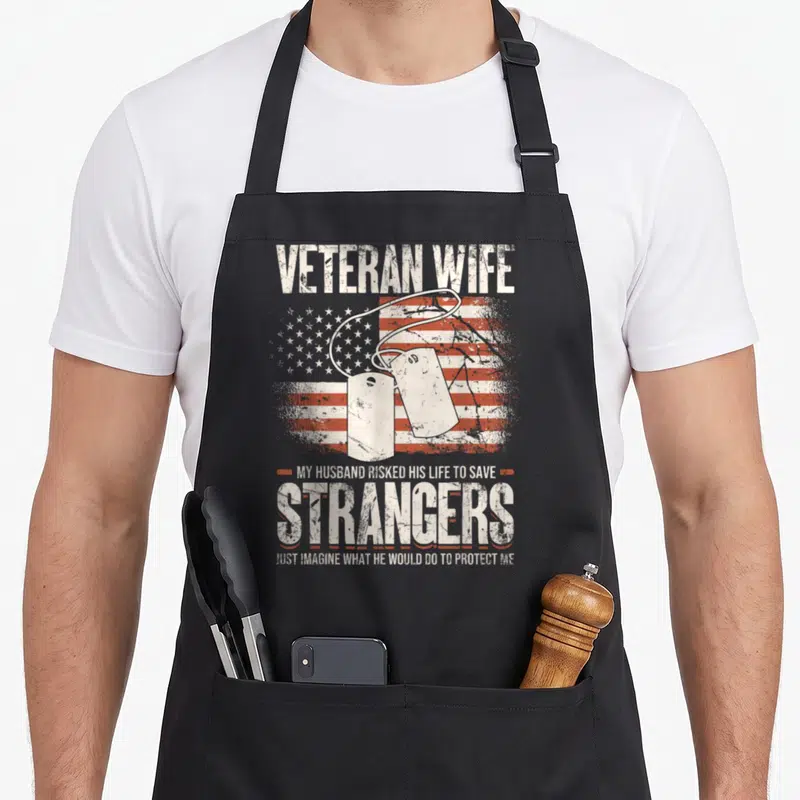 Veteran wife best husband apron - Two dog tags over distressed US flag with quote about husband protecting wife — shown on a black cotton canvas apron against a white background