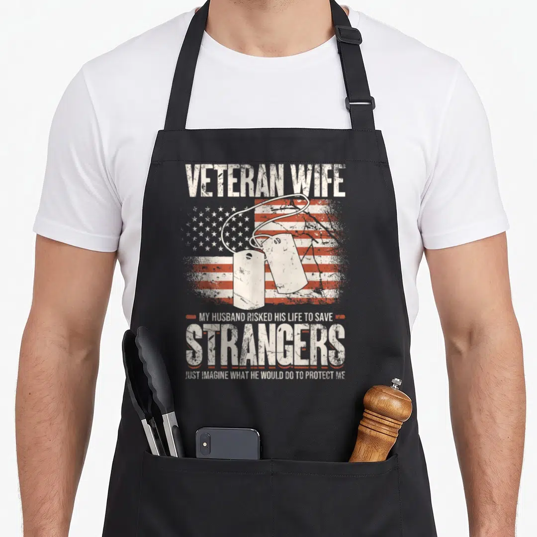 Veteran wife best husband apron - Two dog tags over distressed US flag with quote about husband protecting wife — shown on a black cotton canvas apron against a white background
