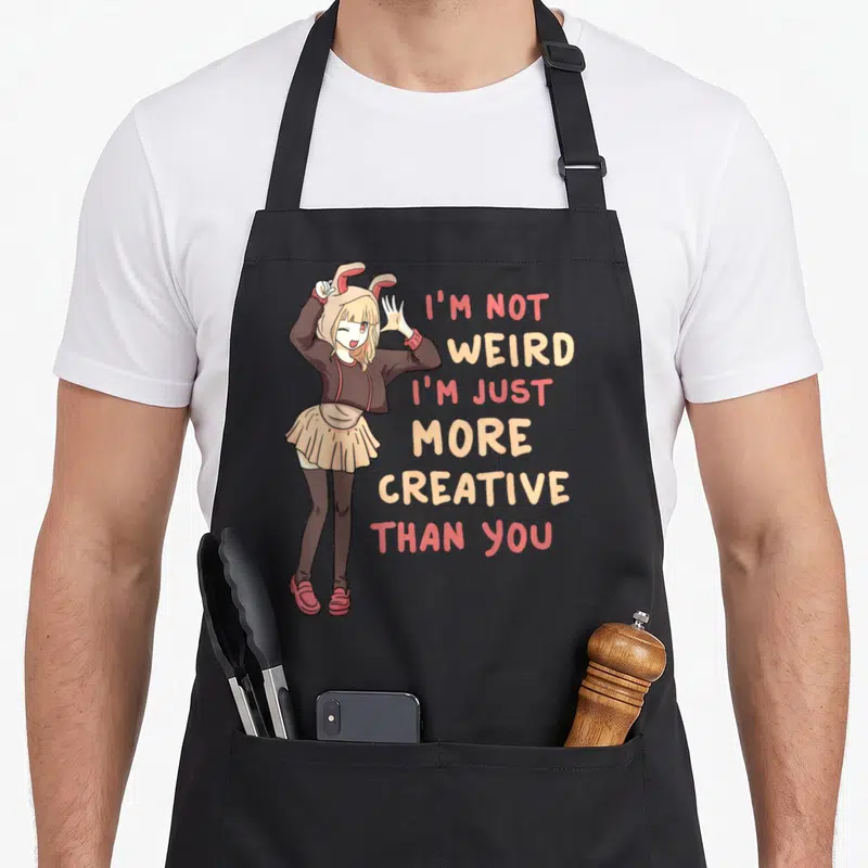 Weird anime apron - Cartoon girl in bunny hat with stacked text I'm not weird I'm just more creative than you — shown on a black cotton canvas apron against a white background