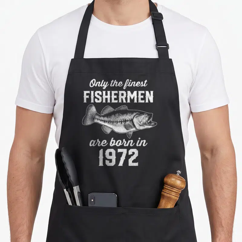 54th fishing aprons - White distressed fish between text Only the finest FISHERMEN are born in 1972 — shown on a black cotton canvas apron against a white background