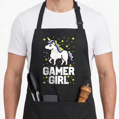 Pixel video game apron - Pixelated white unicorn with rainbow mane and yellow stars above bold gamer girl text — shown on a black cotton canvas apron against a white background