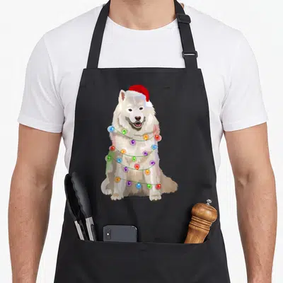 Samoyed christmas lights apron - Realistic white dog sitting facing forward wearing red santa hat wrapped in colorful — shown on a black cotton canvas apron against a white background