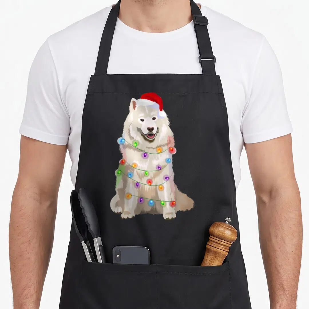 Samoyed christmas lights apron - Realistic white dog sitting facing forward wearing red santa hat wrapped in colorful — shown on a black cotton canvas apron against a white background