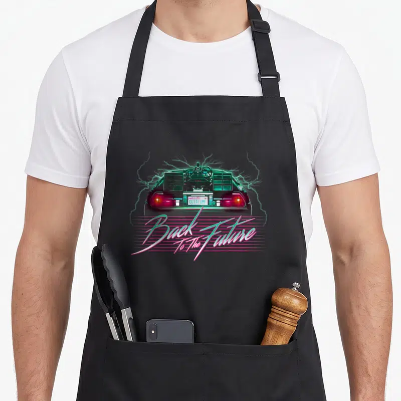 Delorean 80s apron - Rear of DeLorean with teal lightning, pink lines, and Back To The Future text — shown on a black cotton canvas apron against a white background