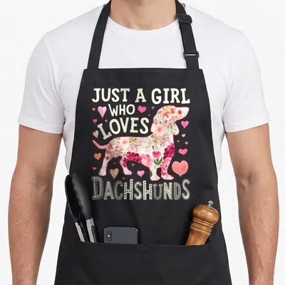Dog dachshund apron - Floral dachshund silhouette with hearts and text Just A Girl Who Loves Dachshunds — shown on a black cotton canvas apron against a white background