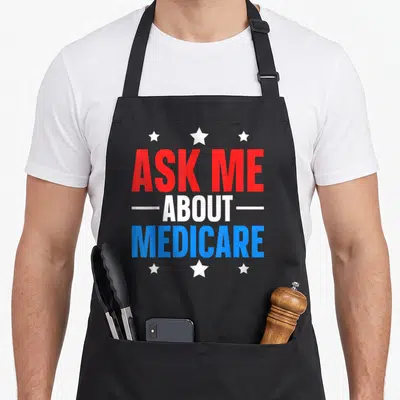 Medicare ask about apron - Stacked red white and blue text reading ASK ME ABOUT MEDICARE framed by six white stars — shown on a black cotton canvas apron against a white background