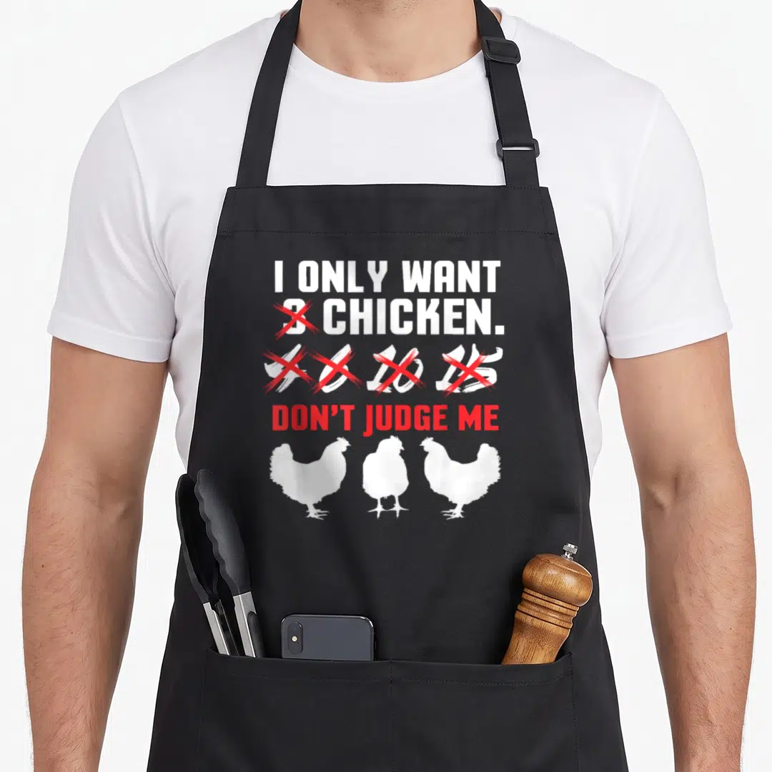 Funny chicken farmer apron - I ONLY WANT 3 CHICKEN text with red X marks and three white chicken silhouettes — shown on a black cotton canvas apron against a white background
