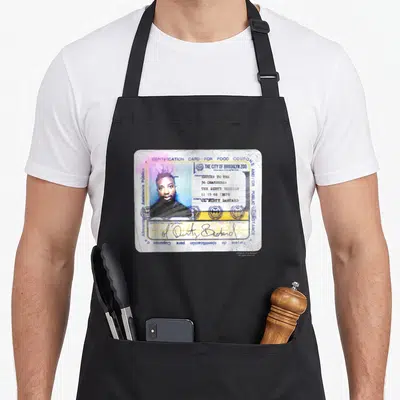 Return the dirty apron - Man's photo on ID card reading Identification Card for Food Coupons and The City of Brooklyn — shown on a black cotton canvas apron against a white background
