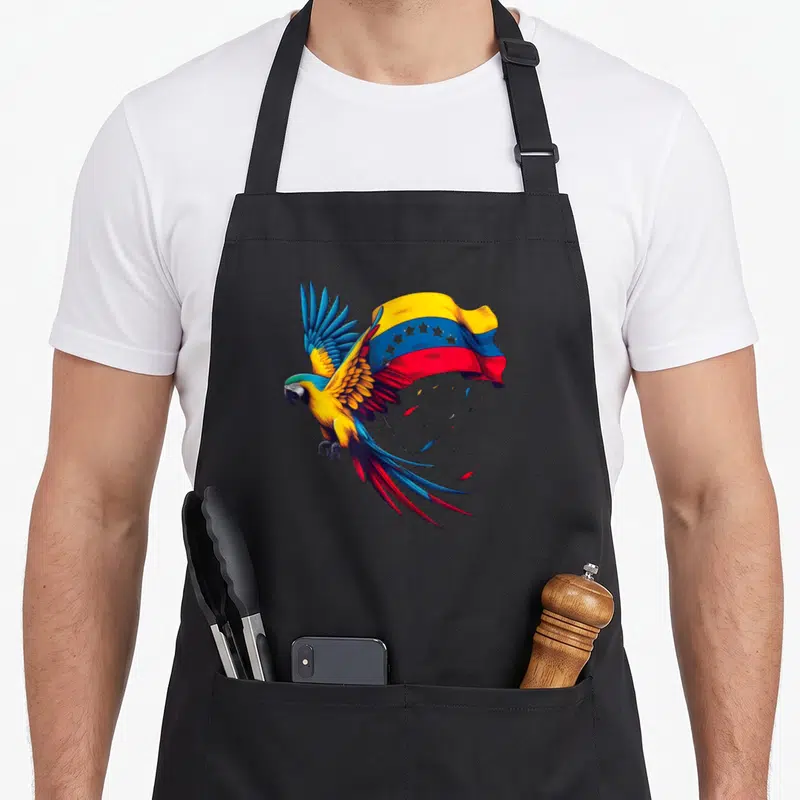 Star venezuela apron - Realistic macaw flying left with Venezuelan flag behind and loose feathers below in yellow blue — shown on a black cotton canvas apron against a white background
