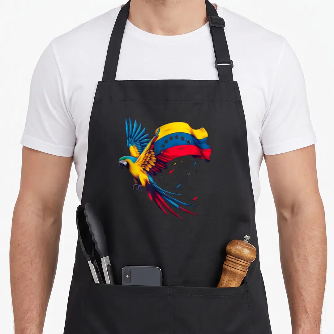 Star venezuela apron - Realistic macaw flying left with Venezuelan flag behind and loose feathers below in yellow blue — shown on a black cotton canvas apron against a white background
