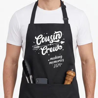 Squad memory apron - White Cousin Crew text with arrow and making memories 2024 surrounded by small stars — shown on a black cotton canvas apron against a white background