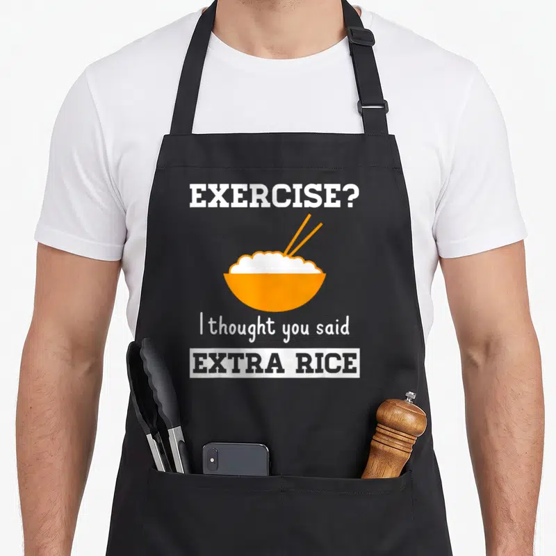 Rice asian apron - Orange bowl of white rice with chopsticks and text EXERCISE? I thought you said EXTRA RICE — shown on a black cotton canvas apron against a white background