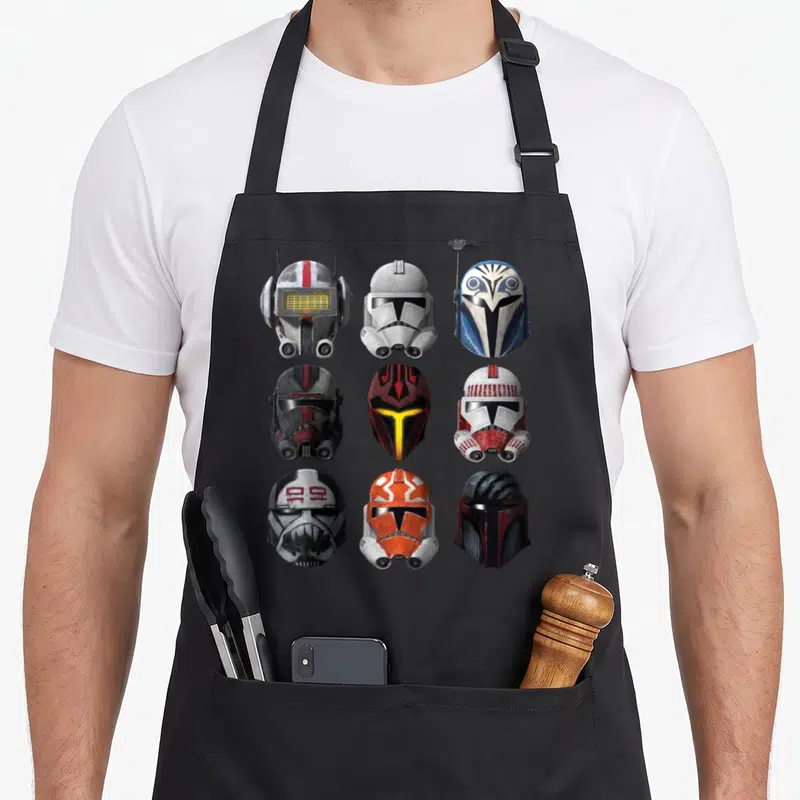 Helmet wars new apron - Nine clone trooper and bounty hunter helmets in a 3x3 grid with white, grey, red, blue, orange — shown on a black cotton canvas apron against a white background