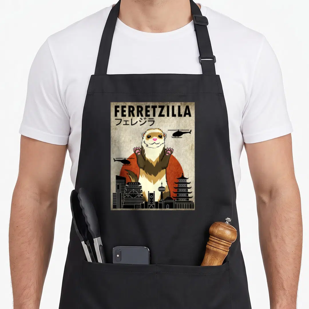 Ferretzilla crazy ferret man apron - Giant cartoon ferret over red sun with helicopters and black skyline featuring — shown on a black cotton canvas apron against a white background