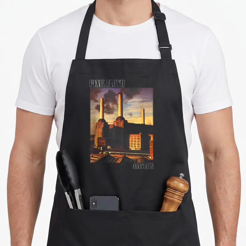 Cover animal apron - PINK FLOYD text above Battersea Power Station with floating pig, ANIMALS text below right — shown on a black cotton canvas apron against a white background