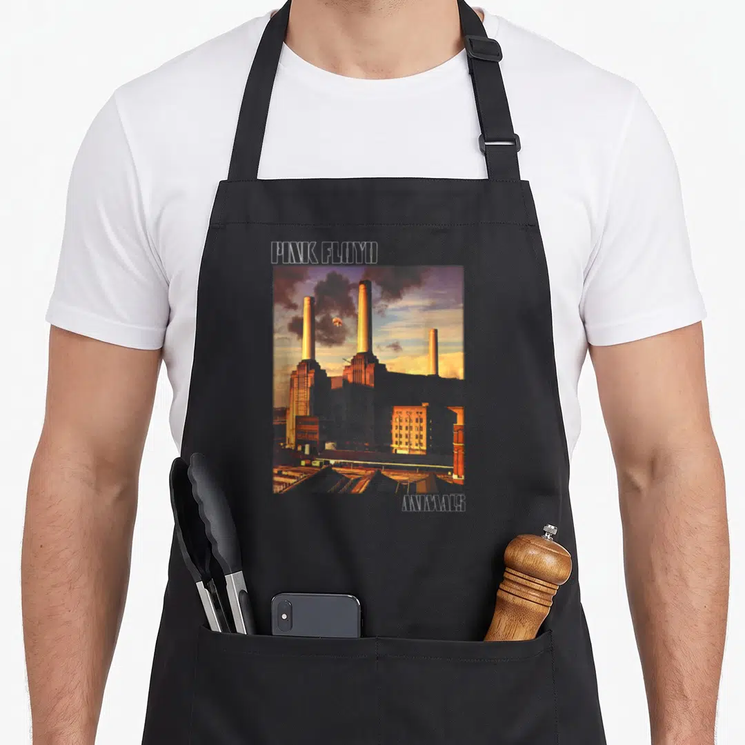 Cover animal apron - PINK FLOYD text above Battersea Power Station with floating pig, ANIMALS text below right — shown on a black cotton canvas apron against a white background