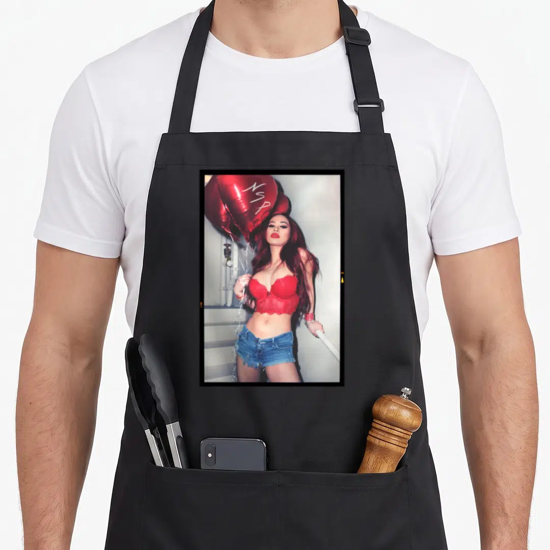 Hot design imports vintage apron - Woman in red bra and denim shorts holding red balloon with NSP written in white — shown on a black cotton canvas apron against a white background