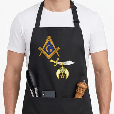 Shriner mason apron - Gold G in blue square and compass above silver scimitar and crescent moon emblem with star — shown on a black cotton canvas apron against a white background