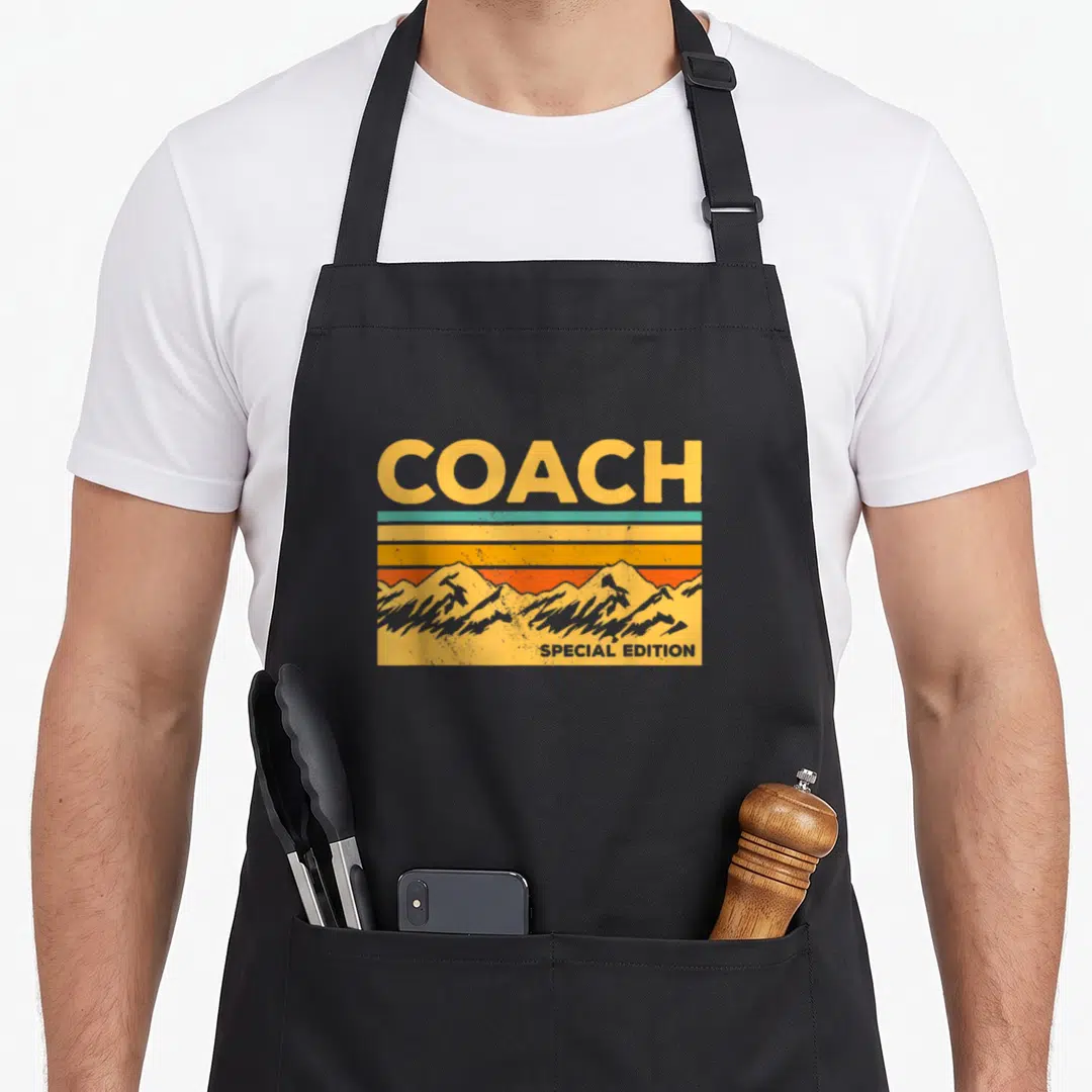 Coach special aprons - COACH SPECIAL EDITION text above retro mountains and yellow orange blue stripes — shown on a black cotton canvas apron against a white background
