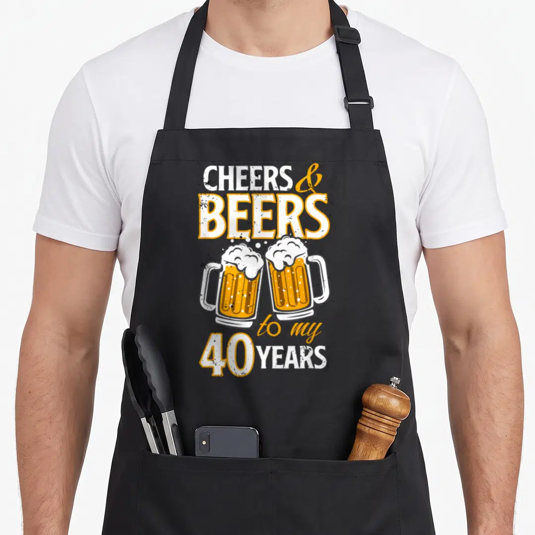 Beer birthday apron - Two clinking beer mugs with distressed text reading CHEERS & BEERS to my 40 YEARS in orange — shown on a black cotton canvas apron against a white background
