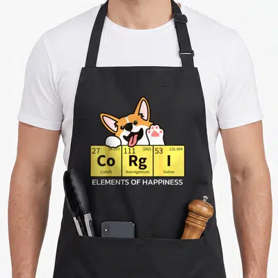 Funny corgi apron - Cartoon corgi head over yellow Cobalt Roentgenium Iodine squares with Elements of Happiness text — shown on a black cotton canvas apron against a white background