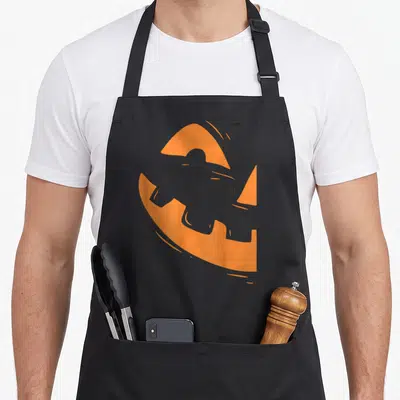 Face couple halloween apron - Stylized orange pumpkin shape with a carved face silhouette in minimalist art style — shown on a black cotton canvas apron against a white background