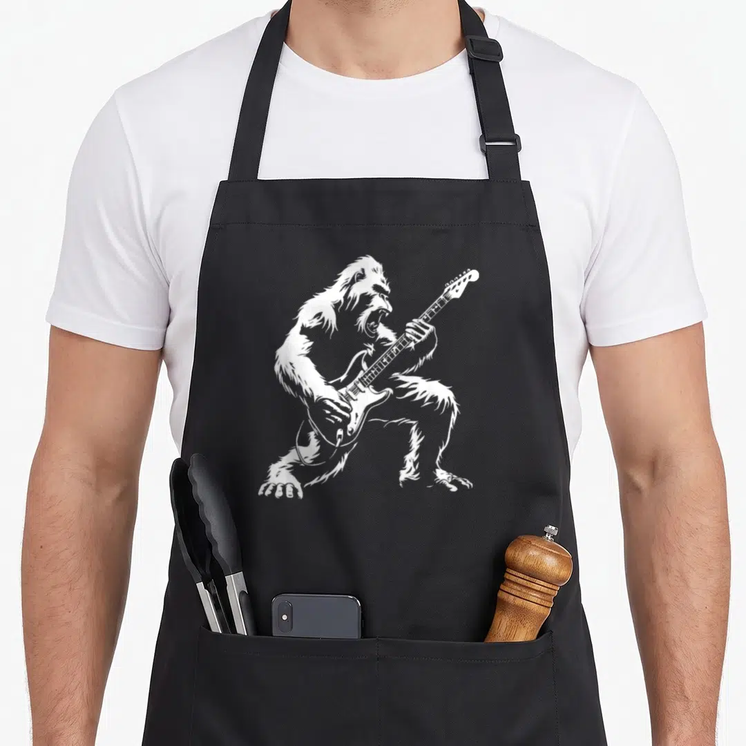 Playing bigfoot apron - White silhouette of a gorilla playing an electric guitar in a rock pose — shown on a black cotton canvas apron against a white background